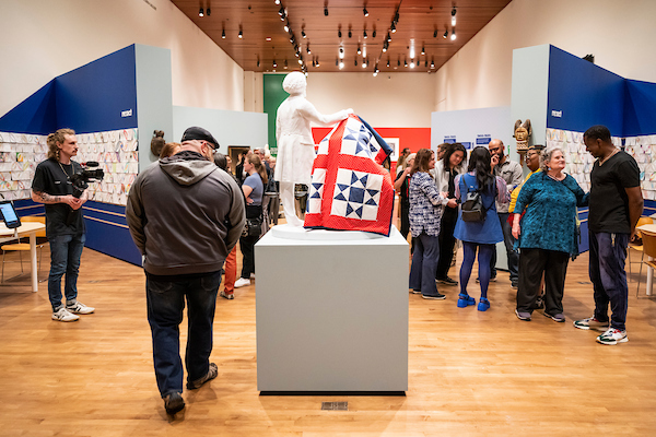Museum visitors gather around a central sculpture on a pedestal in a gallery.