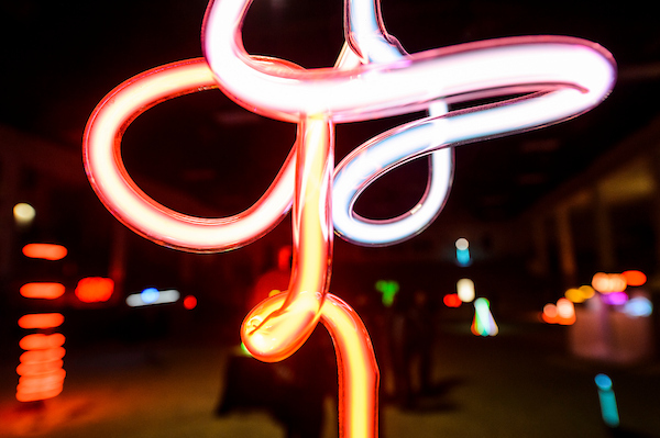 Glowing neon sculpture with looping pink, red, and blue light trails at night.