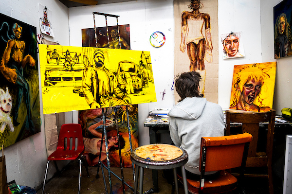 Student works in a painting studio surrounded by colorful artworks and sketches.
