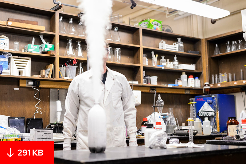 A chemistry demonstration in a lab: a person in a white lab coat stands behind a flask shooting a plume of white vapor. File size: 291 KB.